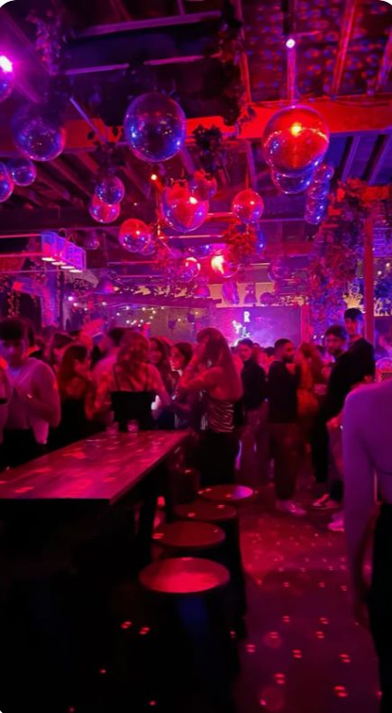 Crowd dancing beneath disco balls and magenta lights